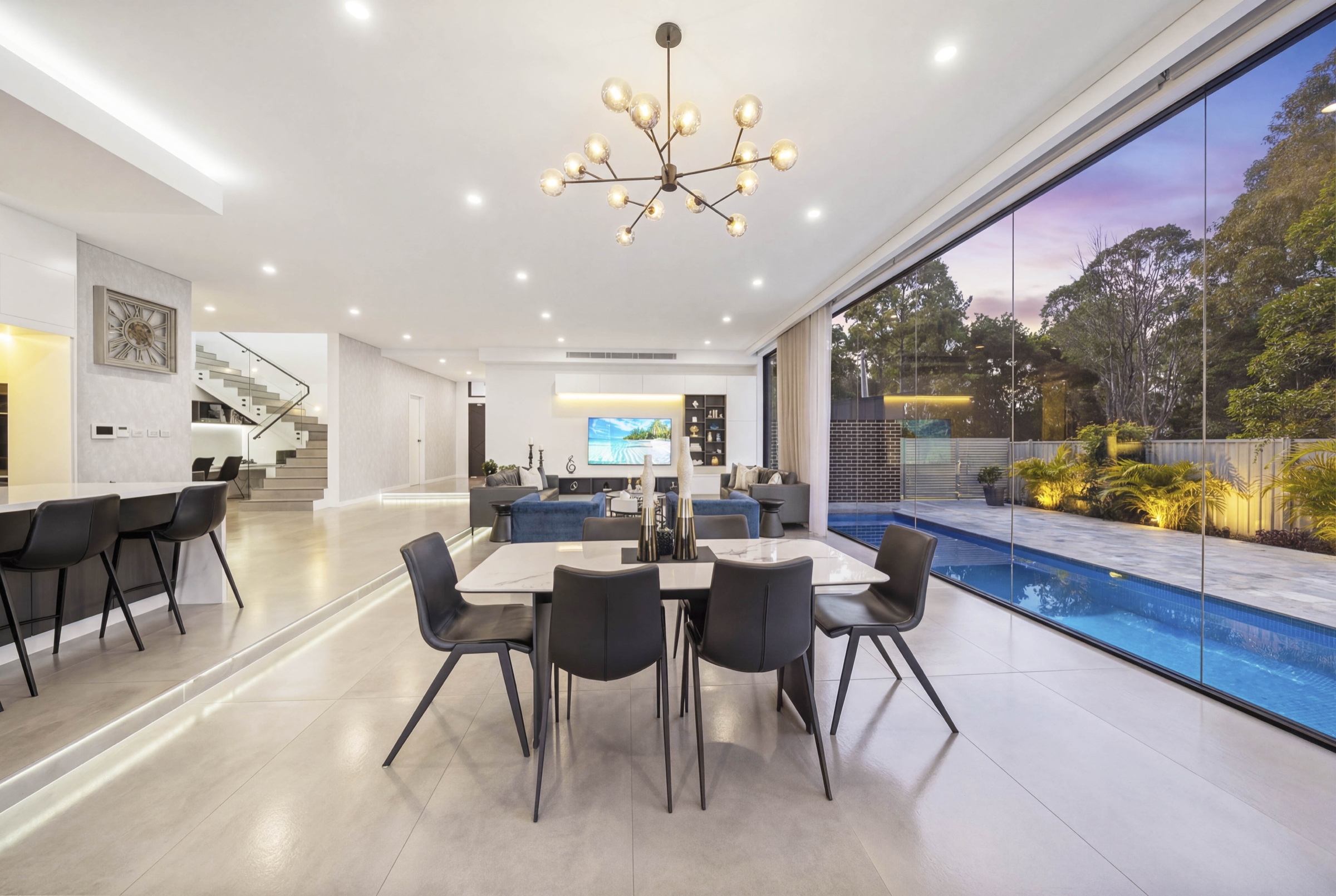 Open-plan living and dining room overlooking a pool at twilight